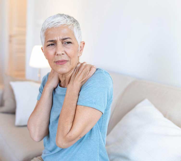 Lady wearing a blue tee, holding her shoulder with both hands from the front.