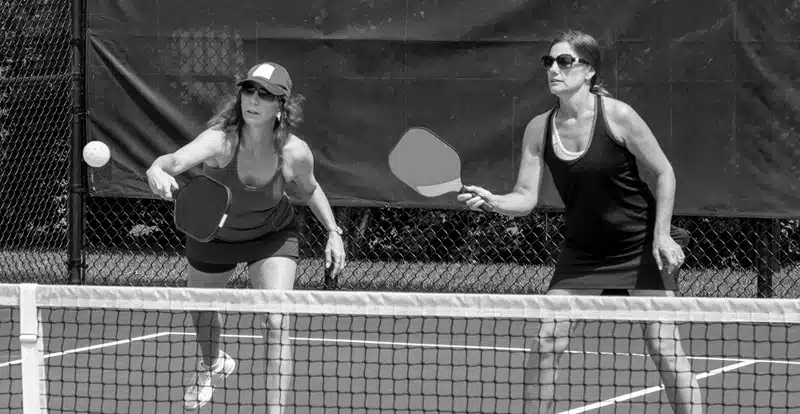 Two women playing pickleball on an outdoor court.